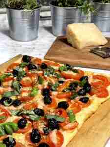 Homemade pizza on puff pastry with a block of parmesan and a vegetable peeler to grate the cheese