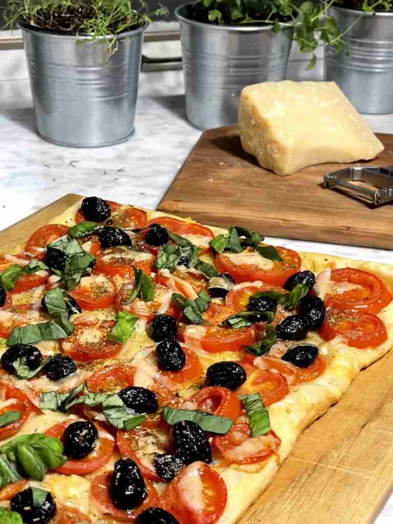 Homemade pizza on puff pastry with a block of parmesan and a vegetable peeler to grate the cheese