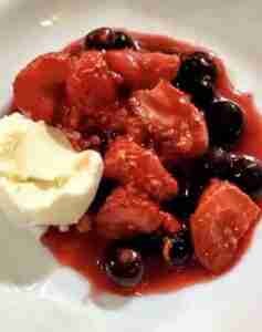 A bowl of fruit soup with a small scoop of vanilla ice cream